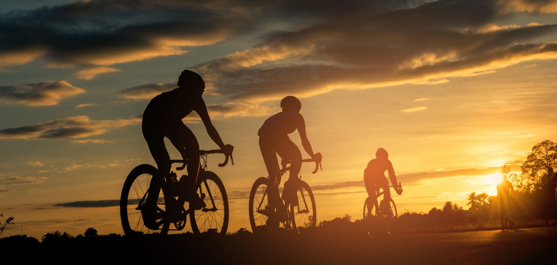 Drie fietsers met helmen rijden de zonsondergang tegemoet